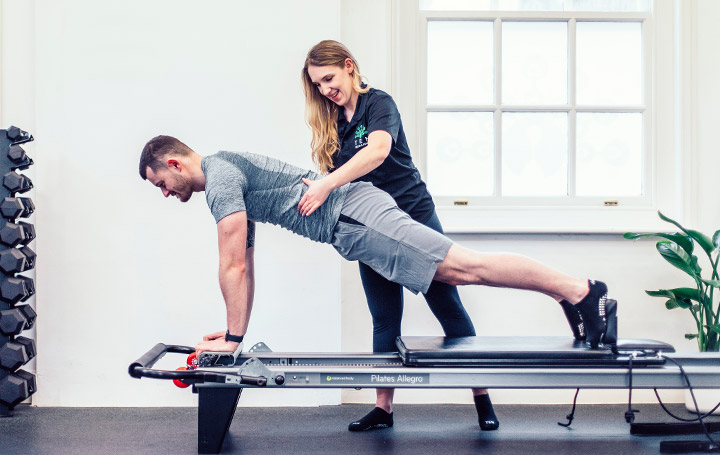 A Reformer Pilates instructor helps a client use the reformer correctly