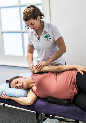 A client sitting upright on a physio table undergoing a postnatal assessment with a Physiotherapist after giving.