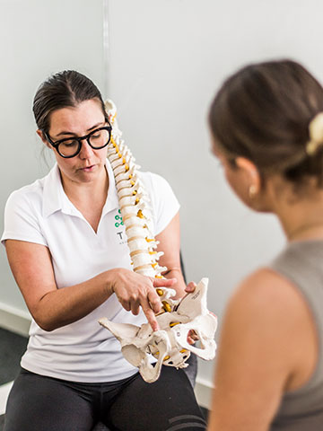 A specialist pelvic health physio demonstrating to a client the area being impacted by their condition, using a spinal/pelvic skeleton model.